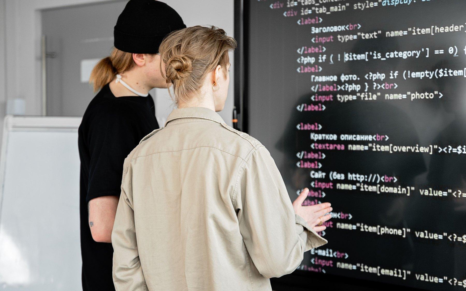 Two developers working through code on a wall screen